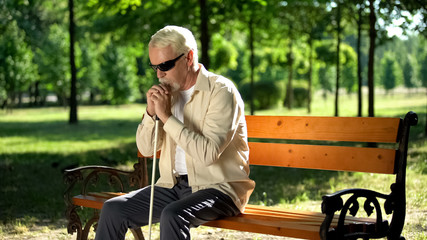 Depressed blind man sitting alone in park, socially disadvantaged population