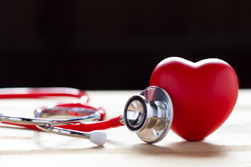 Stethoscope and red heart on wooden table with black background. Cardiology concept or concept of heart health day.