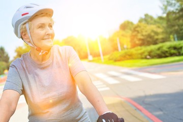 Active senior woman on bicycle with yellow lens flare in background