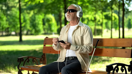 Old blind man putting headset cable in phone, listening voice message, audiobook