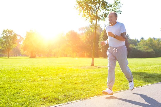 Active Senior Man Running In Park With Yellow Lens Flare In Background