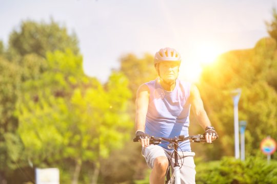 Active Senior Man Riding Bicycle In Park With Yellow Lens Flare In Background