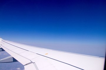 Fototapeta premium View through an airplane window onto the left wing with blue sky and some land on the bottom