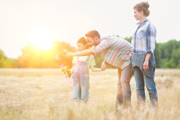 Fototapeta premium Happy family walking in wheat field with yellow lens flare in background