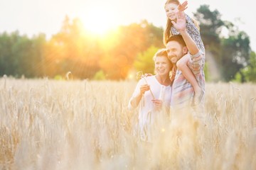 Happy family walking in wheat field with yellow lens flare in background © MDBPIXS