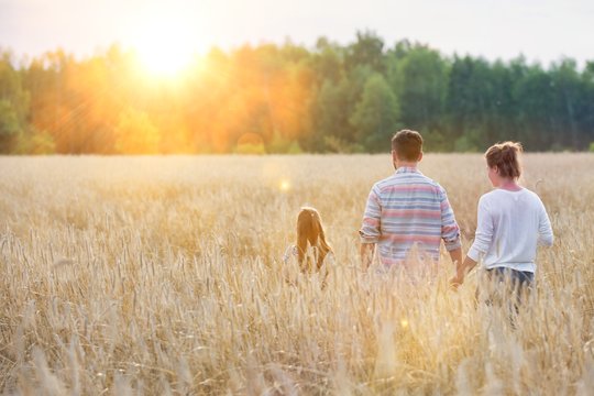 Happy family walking in wheat field with yellow lens flare in background