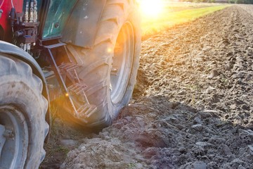 Low angle view of tractor wheel in field with yellow lens flare in background