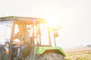 Mature farmer driving tractor in field with yellow lens flare in background