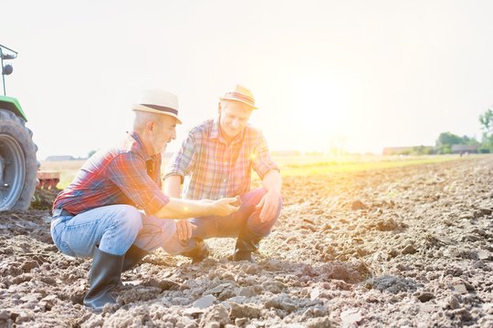 Farmers examining soil in field with yellow lens flare in background