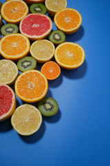 Fresh summer fruits on blue background. Flat lay. Tropical summer mix grapefruit, orange, mandarin, kiwi, lemon. Fruit background with copy space.