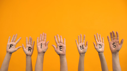 Friends written on palms on orange background, unity connection, assistance