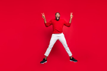 Fototapeta na wymiar Full body photo of excited guy student jumping making v-signs wearing sweater pants trousers isolated over red background