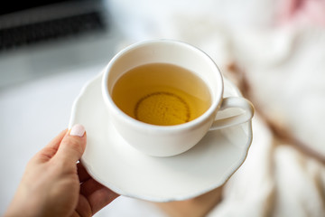 Close-up. Female hands hold a white cup of tea on the background of the bed. Cozy. Autumn. Winter.