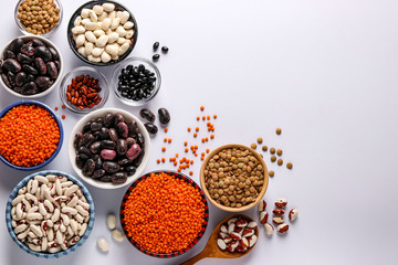 Red and brown lentils, black, brown and white beans are legumes that contain a lot of protein are located in bowls on white background, concept is healthy eating, copy space, horizontal orientation