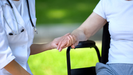 Female therapist holding hand of disabled elderly woman in wheelchair, outdoors