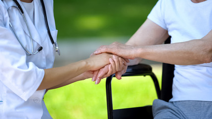 Female nurse holding hand of disabled woman in wheelchair, caring staff