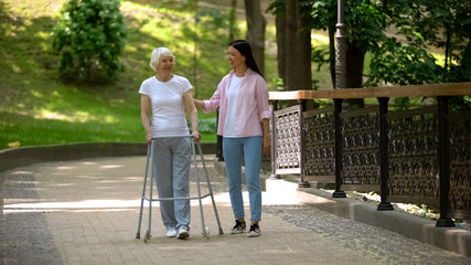 Fototapeta na wymiar Granddaughter supporting disabled grandma with walking frame, day in park