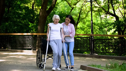 Young woman helping old lady walking on crutches, hip fracture rehabilitation