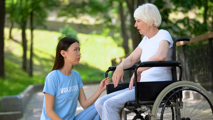 Sick aged woman in wheelchair looking at female volunteer, support and care