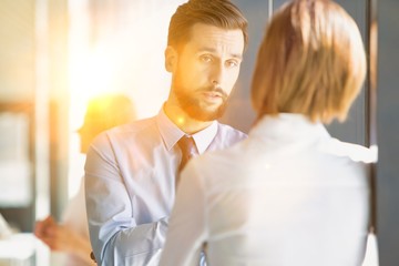 Businessman leaning on wall while talking to businesswoman in office hall