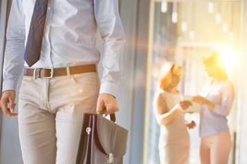 Cropped image of businessman carrying briefcase bag in office hall with yellow lens flare in background