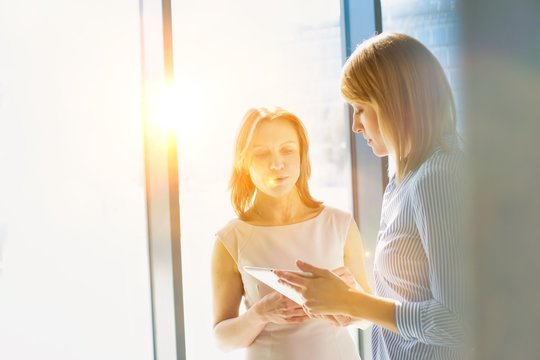 Businesswomen looking at digital tablet in office hall with lens flare in background