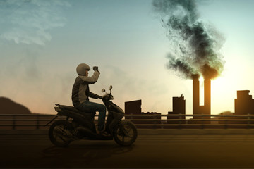 Asian motorcycle taxi man with his motorcycle on the asphalt road with chimney and air pollution from the industrial activity