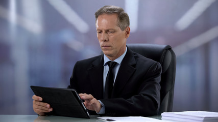 Fototapeta na wymiar Confident male boss working on tablet pc at office desk, online documentation