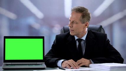 Office manager looking at laptop with green screen, financial app recommendation