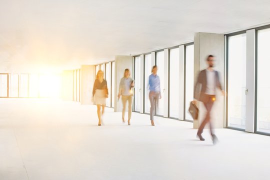 Business People Walking In Office Corridor With Yellow Lens Flare In Background