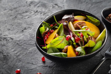 Persimmon salad with pear, pomegranate and pecan. Healthy vegetarian food concept.