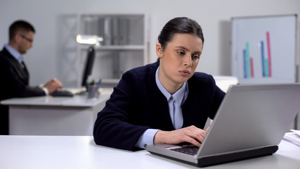 Bored female manager texting on laptop, procrastination issue, avoiding work