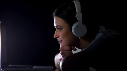 Beautiful girl listening to music in headphones reading social network on laptop