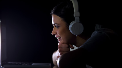 Young woman in headphones sincerely laughing watching funny tv show on laptop