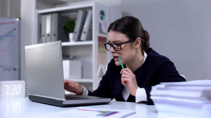 Nervous female chief assistant working on laptop and biting pencil, deadline