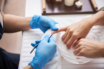 Young lady soaking hands in nail bath while manicurist using stainless nippers