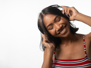 Portrait of happy young Asian girl with headphones dancing over white wall background