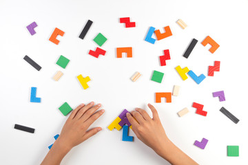 Naklejka premium Kid hand playing with different colorful shapes wooden blocks on white table background. Top view