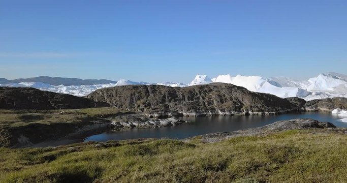 Aerial Forward: Amazing Icebergs Behind Rocky Hills Over Scenic Cove on a Sunny Day, Disko Bay, Greenland