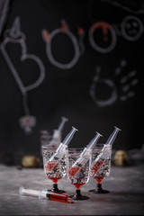 Bloody soda beverage with syringe of red grenadine syrup on dark background. Creepy cocktails for Halloween party.