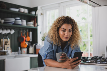 Adult female looking at smartphone whilst having morning coffee