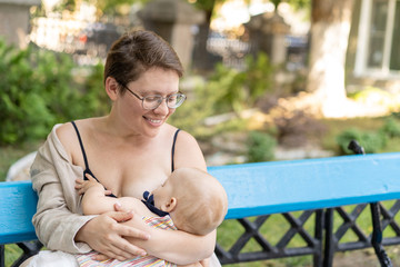 Woman mother breastfeeding her baby outdoors in summer park. Happy motherhood.