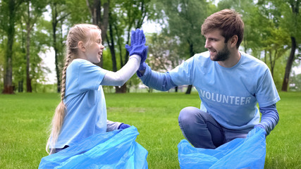 Male volunteer and daughter collecting garbage forest together, giving high five
