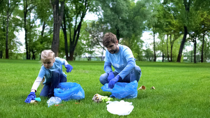 Father and daughter picking up litter in park, participating volunteer project