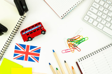 Flat lay frame student desktop with blank spiral notepads, earphones, British bus toy and Britsh flag. Top view language learning concept