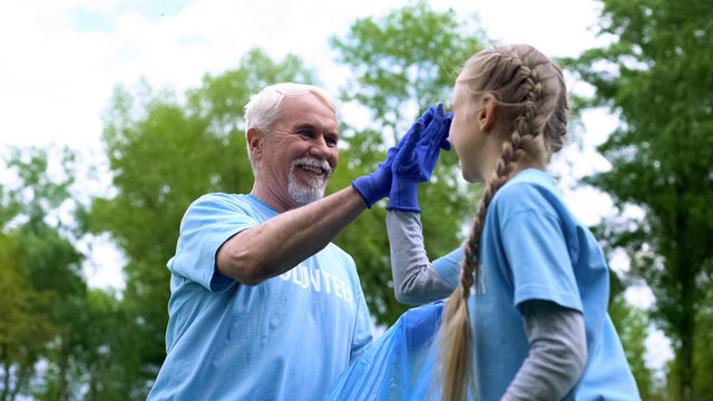 Smiling elderly volunteer with granddaughter collecting garbage giving high five