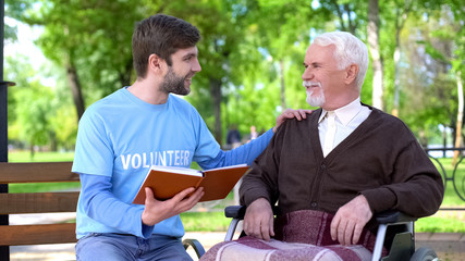 Social worker reading book for disabled pensioner, leisure in park, volunteering