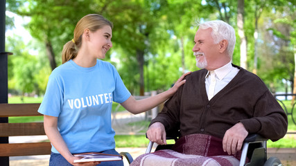 Female volunteer holding book spending time with handicapped elderly man at park