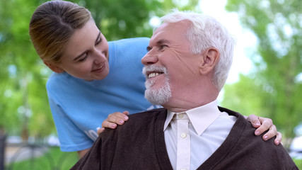 Smiling female volunteer comforting handicapped elderly man at hospital park