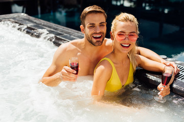 Fototapeta premium sexy couple holding glasses of red wine embracing in swimming pool in sunny day